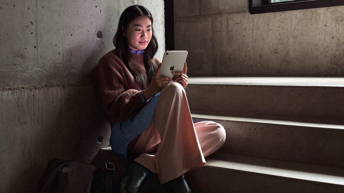 A person holding the new iPad mini while sitting on steps.